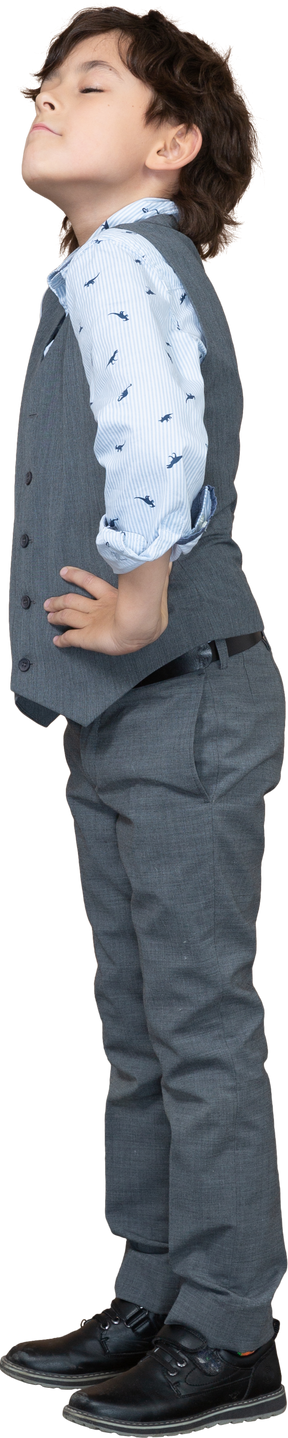 엉덩이에 손으로 포즈를 취하는 회색 양복에 귀여운 소년의 측면보기