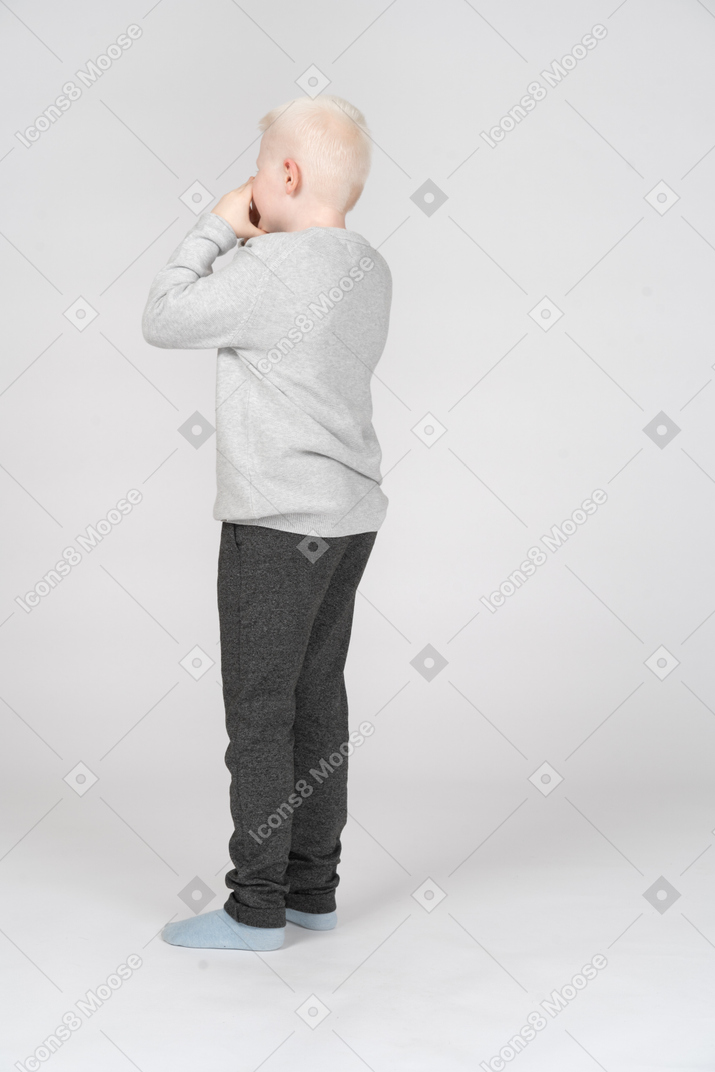 Three-quarter back view of a boy covering his mouth with hands