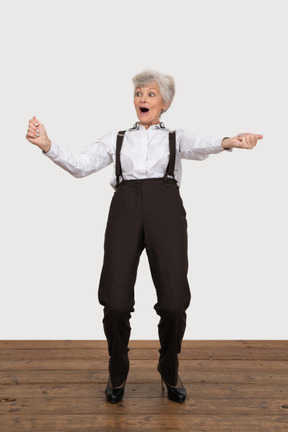 Front view of a happy old lady in office clothing raising hands while screaming