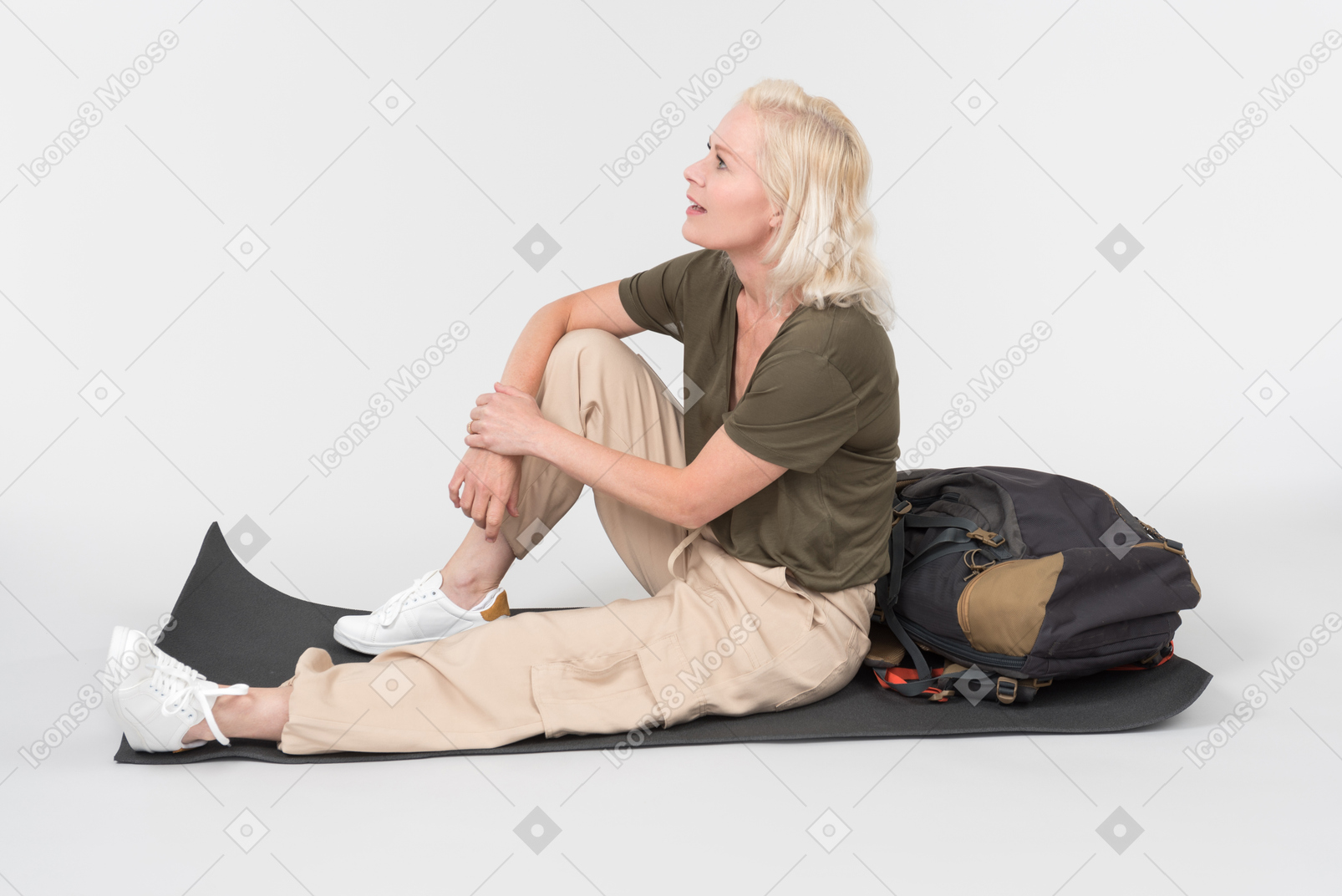Mature female tourist sitting on tourist mat near tourist backpack