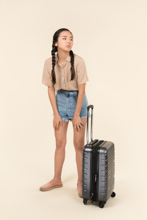 Tired young female traveller standing near suitcase