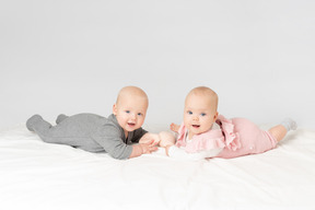 Babyzwillinge, die auf dem magen liegen und angefülltes spielzeug halten