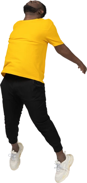 Three-quarter view of a jumping young dark-skinned man in yellow t-shirt outspreading hands