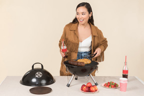 Junge asiatische frau hält eine flasche cola und macht einen grillabend