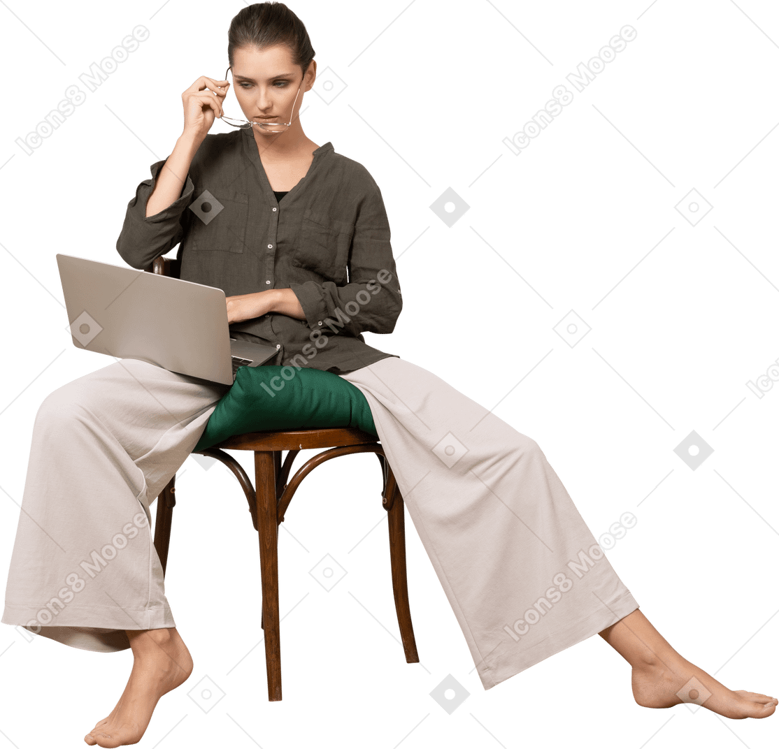 一位穿着家居服的年轻女子坐在椅子上，拿着笔记本电脑，戴上眼镜的前视图