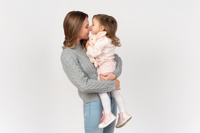 Baby girl sitting in her mother's arms and kissing her