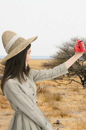 A woman in a hat taking selife with red camera
