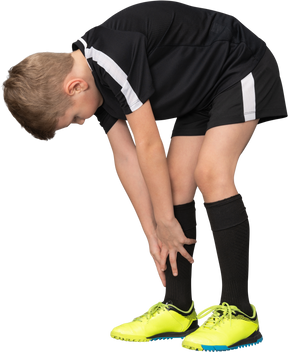 四分之三的儿童男孩穿着足球制服向前倾斜，touching着脚尖