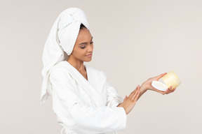 Негритянка в белом халате и головном полотенце наслаждается рутиной ухода за кожей