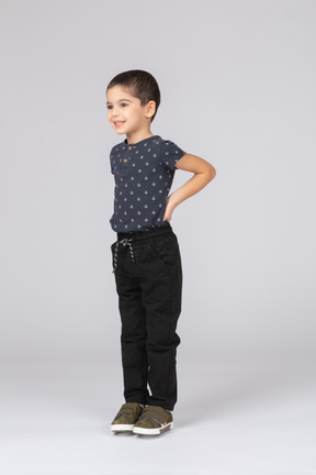 Vista lateral de un niño feliz en ropa casual posando con las manos detrás de la espalda