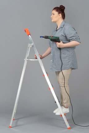 Woman standing sideways on stepladder and holding screw driver