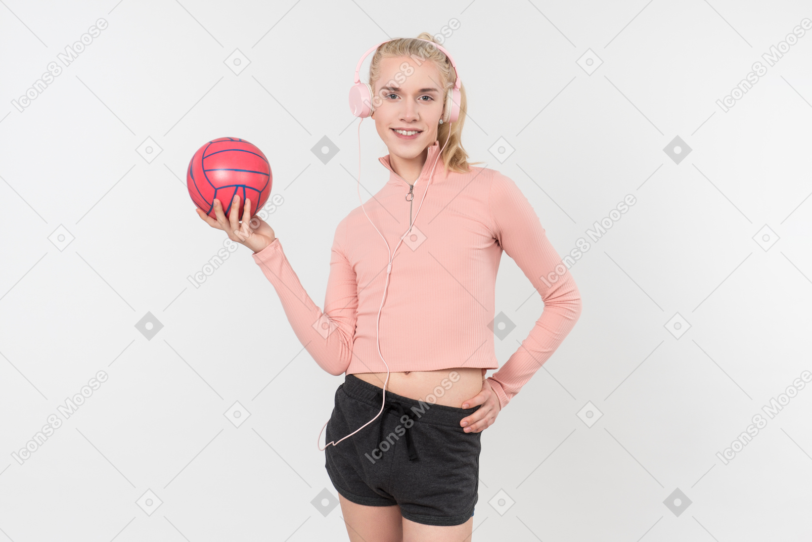 Young blond-haired person in black and pink outfit posing with sports  items against a light grey background