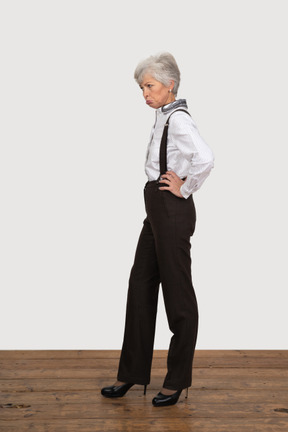 一个不高兴的老太太，把手放在臀部上的办公服装的侧视图
