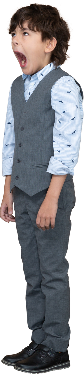 Vista frontal de un niño con traje gris de pie con la boca abierta y mirando hacia arriba