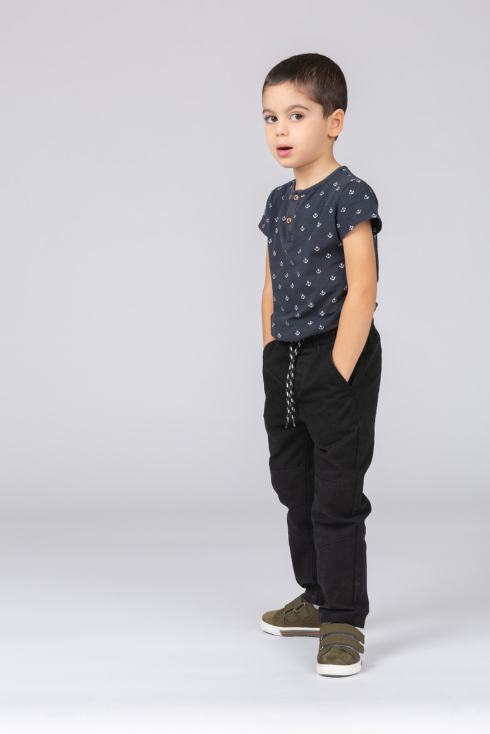 Front view of an impressed boy posing with hands in pockets and looking at camera
