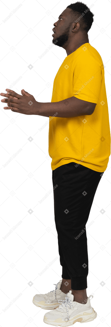 Side view of a young shocked dark-skinned man in yellow t-shirt raising hands