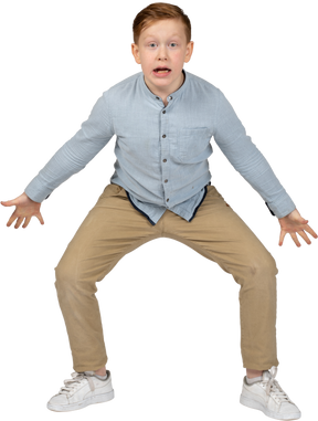 Front view of a boy squatting with outstretched arms and looking at camera