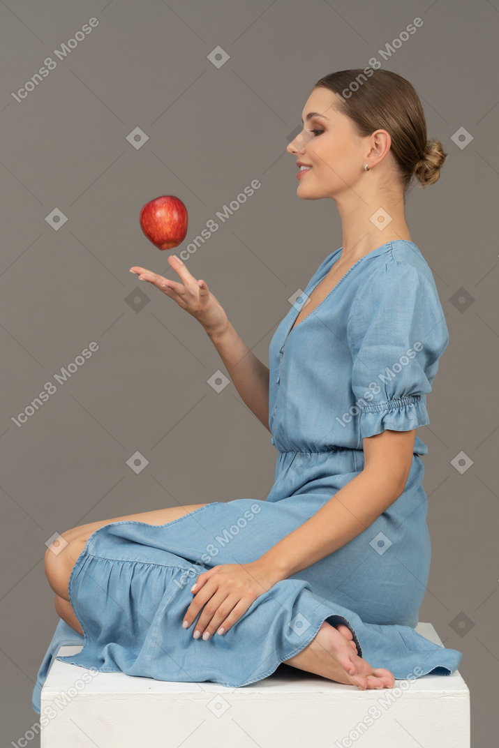 Side view of cheerful young woman tossing apple