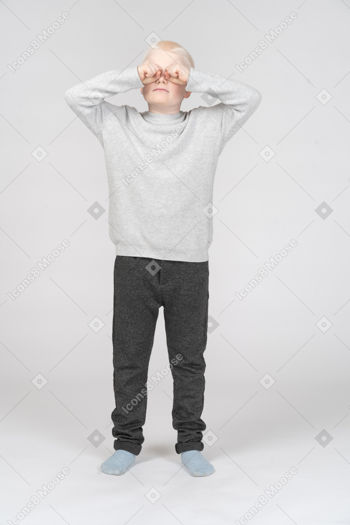 Front view of a boy rubbing eyes with his fists