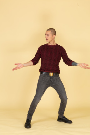 Front view of a young man in red pullover standing with his legs and arms widespread