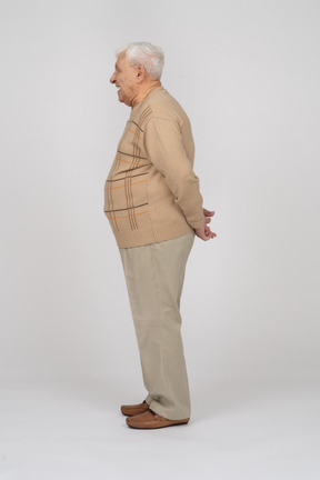 Vista lateral de un anciano con ropa informal de pie con las manos detrás de la espalda